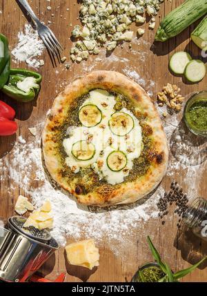 Pizza napoletana con formaggio roquefort, pesto, zuquini e noce. Servito su un tavolo di legno e circondato da tutti gli ingredienti. Scena di preparazione. Foto Stock