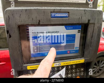 Strasburgo, Francia - Mar 31, 2022: POV maschio mano guardando Parkeon parchimetri con display digitale che mostra l'avviso di pagamento dematerializzato per il parcheggio multa Foto Stock