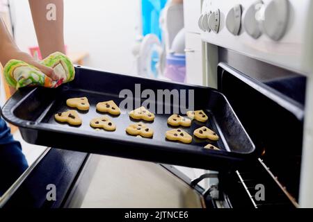 Niente di meglio dei biscotti appena sfornati. Una donna irriconoscibile che prende i biscotti da un forno. Foto Stock