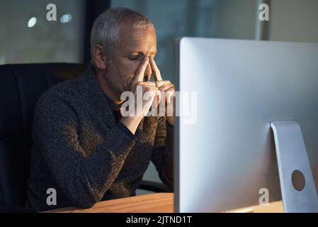 Cercando di mantenere la calma sotto pressione. Un uomo d'affari maturo che guarda stressato mentre lavora tardi in ufficio. Foto Stock