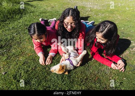 Madre con le sue due figlie, giocando con un cucciolo di recupero d'oro nel parco. Famiglia femminile Foto Stock