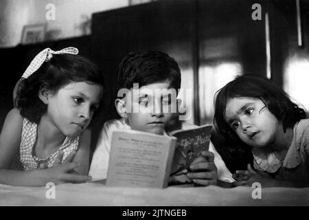 1954 , Bombay , INDIA: Il celebrato britannico nato in india Sir SALMAN RUSHDIE ( nato il 19 giugno 1947 ) quando era giovane ragazzo di 7 anni , leggendo il libro PETER PAN , una favola di James Matthew Barrie , alle sue sorelle SAMEEN e NEVID . Fotografo sconosciuto. - STORIA - FOTO STORICHE - personalità da giovane giovani - personalità quando era giovane - RITRATTO - ritratto - ritratto - SCRITTORE - LETTERATURA per l'INFANZIA - BAMBINO - BAMBINI - LETTERATURA - libro - sorelle - sorelle - fratelli - fratelli - famiglia - famiglia - famiglia - famiglia - FIABA - FIABA --- ARCHIVIO GBB Foto Stock