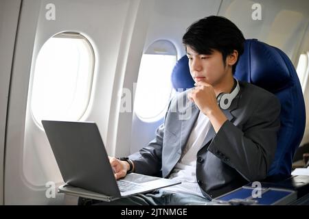 Un uomo d'affari asiatico intelligente e bello o un dirigente maschile che si concentra sul lavoro e sul controllo del suo progetto aziendale sul notebook durante il Foto Stock