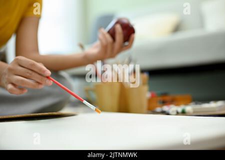 Artista femminile di talento che tiene il pennello, disegnando e dipingendo la sua opera su un poster di tela vuoto. Immagine ritagliata e ravvicinata Foto Stock