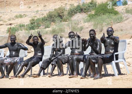 MAR MORTO, GIORDANIA: 18 APRILE 2014. Un gruppo di giovani africani che prendono il bagno di fango al sole sulla spiaggia del Mar Morto. Foto Stock