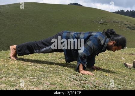Vista laterale a tutta lunghezza di un bel giovane indiano dai capelli lunghi che fa le salse in montagna Foto Stock