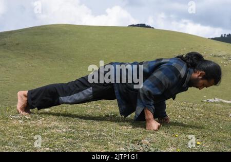 Vista laterale di un giovane indiano dall'aspetto buono che fa il pugno in montagna Foto Stock