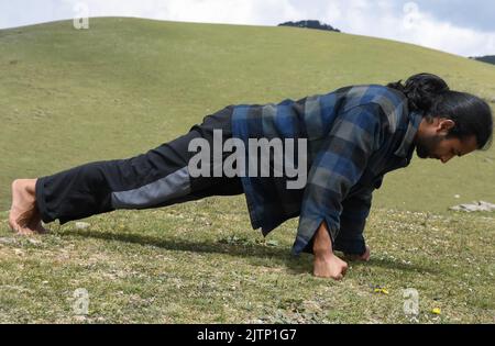 Vista laterale di un giovane indiano dall'aspetto buono che fa il pugno in montagna Foto Stock