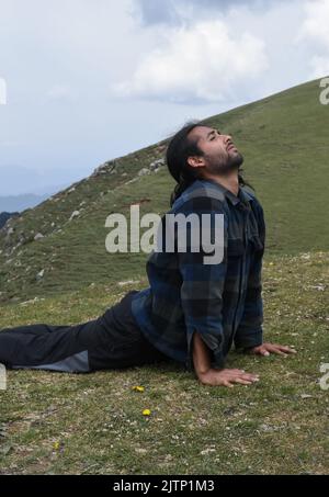 Un bel giovane indiano dai capelli lunghi che fa posa Cobra (posa Bhujangasana Yoga) in montagna Foto Stock