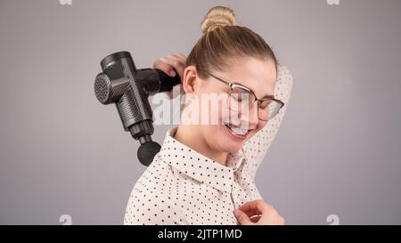 Donna sorridente con bretelle usa una pistola massaggiatore per la schiena. Foto Stock