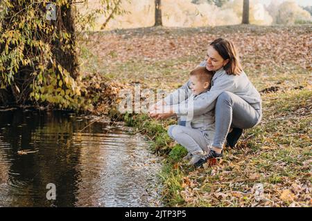 La madre gioca con suo figlio sul bordo di un lago imitando la pesca di un pesce grande e pesante con una canna. Paesaggio forestale naturale. Bellezza naturale Foto Stock