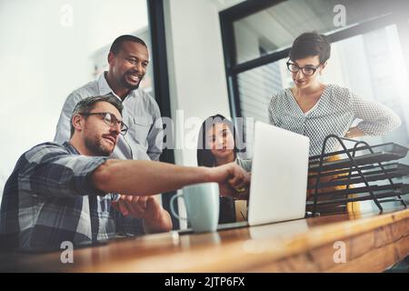 Il suo team è sempre pronto e disponibile ad aiutare. Inquadratura ad angolo basso di un gruppo di uomini d'affari riuniti intorno a un notebook in ufficio. Foto Stock