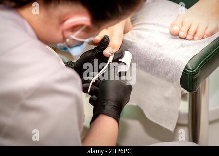 Pedicure professionale. Pedicure master indossare guanti in lattice taglia le unghie femminili nel salone di bellezza, primo piano Foto Stock