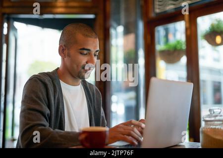 Questo è il suo ambiente di lavoro perfetto per rimanere produttivo. Un giovane uomo che lavora sul suo computer portatile in un bar. Foto Stock