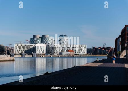 Copenaghen, Danimarca. Agosto 13, 2022. Donna che fa jogging accanto al fiume a Copenaghen con gli edifici della città delle Nazioni Unite sullo sfondo Foto Stock