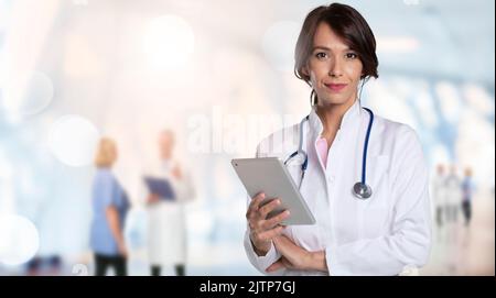 Donna sorridente medico tenendo la clipboard in mano mentre si è in piedi in clinica. Squadra medica irriconoscibile in piedi sullo sfondo. Spazio di copia. Foto Stock