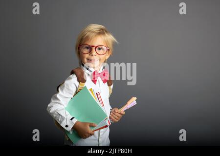 Carino bambino biondo prescolare, ragazzo, tenendo libri e notebook, mela, indossare occhiali, pronto per andare a scuola Foto Stock