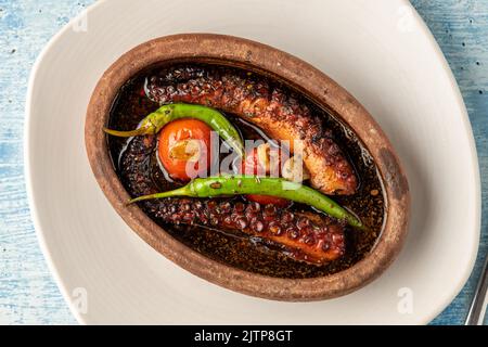 Polpo in casseruola con pomodori e peperoni su fondo di pietra blu Foto Stock