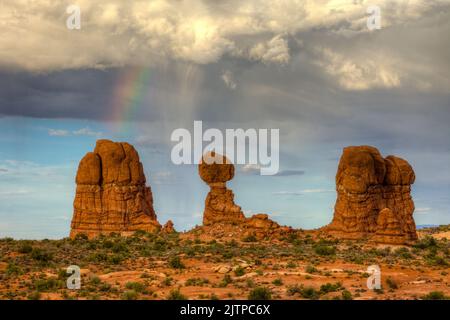 Virga e un arcobaleno su Balanced Rock nel Parco Nazionale di Arches, Moab, Utah. Foto Stock