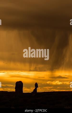 Silhouette al tramonto di Balanced Rock con virga da una pioggia sul parco nazionale di Arches, Moab, Utah. Foto Stock