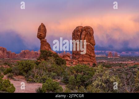 Nuvole colorate di tempesta nella luce post-tramonto su Balanced Rock nel Parco Nazionale di Arches, Moab, Utah. Foto Stock