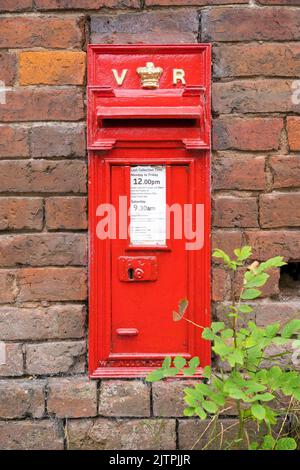 Primo piano di una tradizionale casella postale reale di Victoria Regina (VR), rossa, situata in un vecchio muro di mattoni nella campagna del Regno Unito. Foto Stock