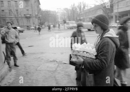 Bucarest, Romania, gennaio 1990. Meno di un mese dopo la rivoluzione anticomunista del dicembre 1989, la gente ha ancora avuto un momento difficile ottenere il possesso di generi alimentari di base. Il sistema economico socialista centralizzato ha creato scarsità e fame. In questa immagine, una donna cammina con una grande quantità di uova. La gente tendeva a comprare più di quanto ne aveva bisogno, impaurita di non trovare più cibo. Foto Stock