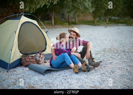 passeggiate nella natura. coppia di amanti sedersi e parlare in campeggio vicino tenda sul lato del fiume Foto Stock