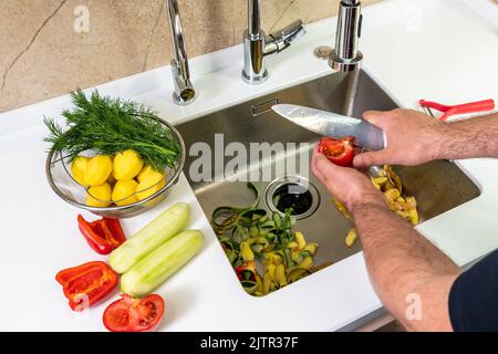 Taglio del pomodoro, sbucciatura e taglio delle verdure fresche in cucina Foto Stock