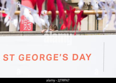 Uno spettatore è visto dietro le decorazioni mentre le persone si riuniscono per le celebrazioni del giorno di San Giorgio a Trafalgar Square, nel centro di Londra. Foto Stock