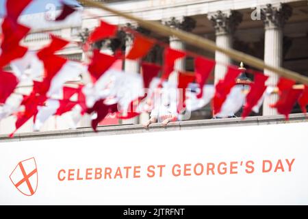 Uno spettatore è visto dietro le decorazioni mentre le persone si riuniscono per le celebrazioni del giorno di San Giorgio a Trafalgar Square, nel centro di Londra. Foto Stock