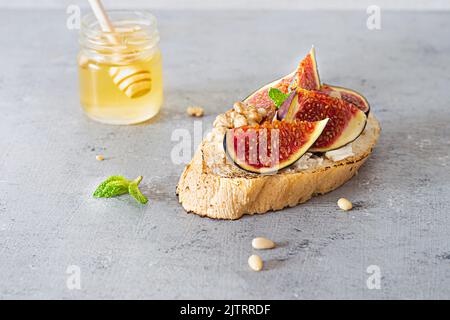 Bruschetta croccante con ricotta morbida, fichi maturi, noci e pinoli, menta e miele su sfondo chiaro. Foto Stock