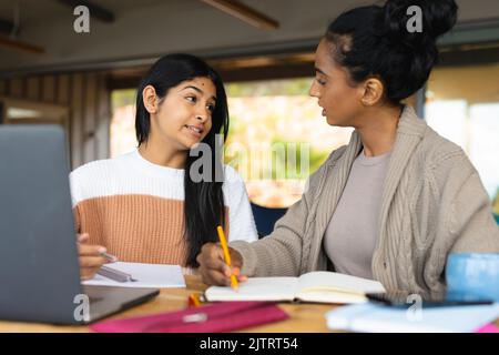 Madre biraciale che scrive nel libro mentre insegna figlia adolescente sul tavolo a casa Foto Stock