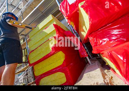 Il capo sovrintende, controlla i lavori in cantiere. Confezioni di materiale termoisolante, lana di roccia avvolta in foglio collocato sul cantiere. Foto Stock