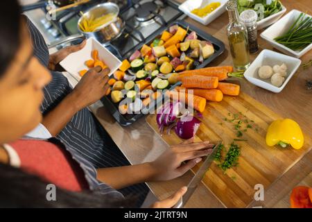 Vista ad angolo alto della figlia biraciale e della madre che tagliano verdure fresche sul tagliere in cucina Foto Stock