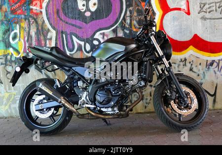 Rheine, NRW, Germania - Agosto 24 2022 Una motocicletta nera Suzuki SV650 in piedi di fronte a una parete di graffiti Foto Stock