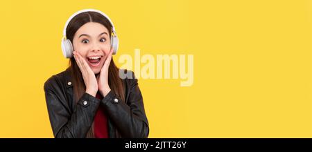 bambino stupito in cuffie su sfondo giallo. Ritratto per bambini con cuffie, poster orizzontale. Ragazza che ascolta musica, banner con spazio copia. Foto Stock