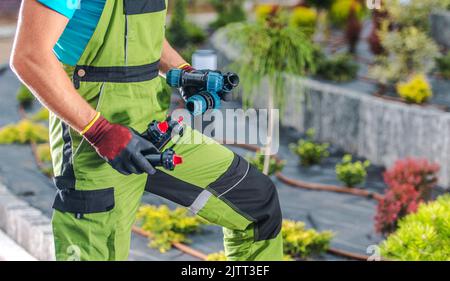 Paesaggista professionale tenendo connettori e sprinkler nelle mani durante la costruzione e l'installazione di un sistema di irrigazione per gocciolamento da giardino per garantire la funzionalità automatica Foto Stock