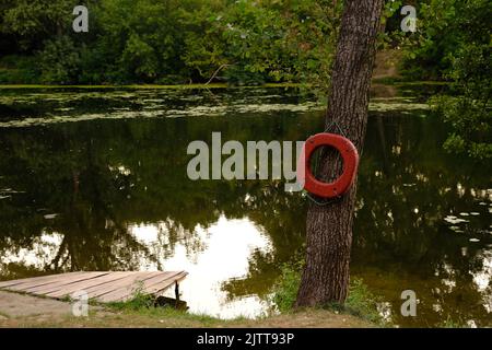 Anello di Lifebuoy sull'ormeggio del fiume con molo in legno all'aperto. Foto Stock