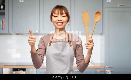 donna felice in grembiule con cucchiaio di legno e spatola Foto Stock