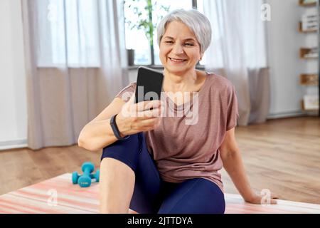 donna anziana con smartphone che si esercita a casa Foto Stock