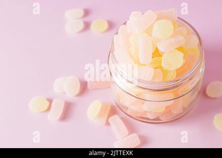 Caramelle gommose agli agrumi masticabili in vasetto di vetro su sfondo rosa pastello. Vista dall'alto, messa a fuoco selettiva. Foto Stock