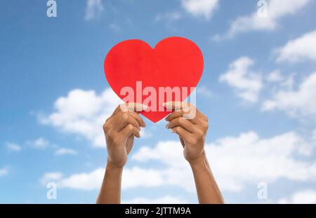 primo piano delle mani che tengono il cuore rosso sopra il cielo blu Foto Stock