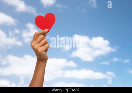 primo piano della mano che tiene il cuore rosso sopra il cielo blu Foto Stock