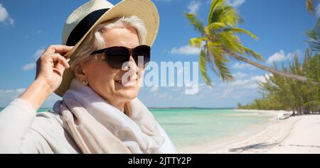 Felice donna senior in occhiali da sole e cappello sulla spiaggia Foto Stock
