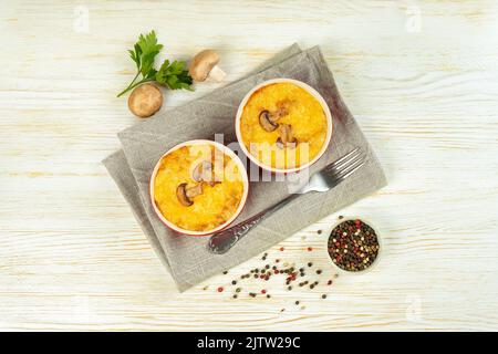 Casseruola di pollo e funghi con crosta dorata, julienne con formaggio al forno, gratin cremoso in parte ramekin creta pentola su fondo di legno bianco. FR Foto Stock