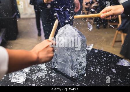 Processo di rottura del ghiaccio con martello e raccogli ghiaccio, gruppo di persone che distruggono il cubo di ghiaccio frantumato, concetto di successo del lavoro di squadra, concetto di partenza pari Foto Stock