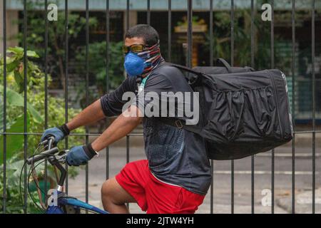 Uomo nero che consegna il cibo in bicicletta in una strada a Rio de Janeiro, Brasile. Foto Stock