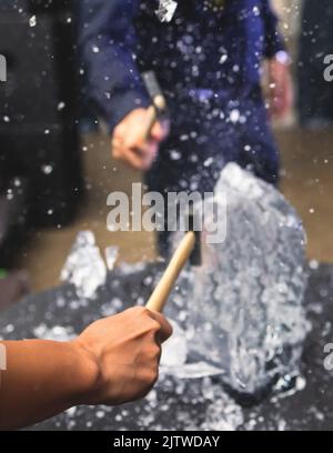 Processo di rottura del ghiaccio con martello e raccogli ghiaccio, gruppo di persone che distruggono il cubo di ghiaccio frantumato, concetto di successo del lavoro di squadra, concetto di partenza pari Foto Stock