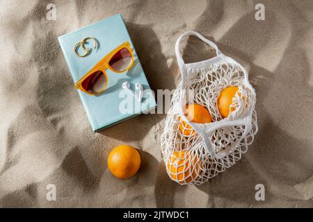 borsa di arance, auricolari e occhiali da sole sulla spiaggia Foto Stock